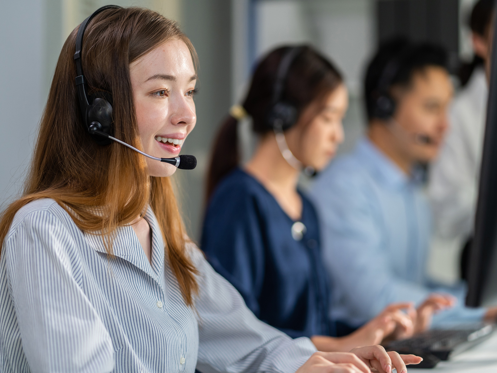 Callcenter-Team im modernen Großraumbüro mit Holzakzenten, Schreibtischen, Monitoren und Headsets in heller Atmosphäre