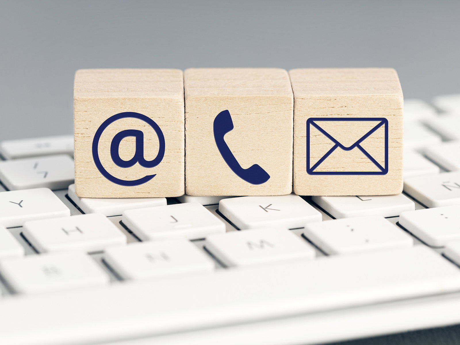 Holzwürfel mit Symbolen für E-Mail, Telefon und Nachricht auf einer Tastatur