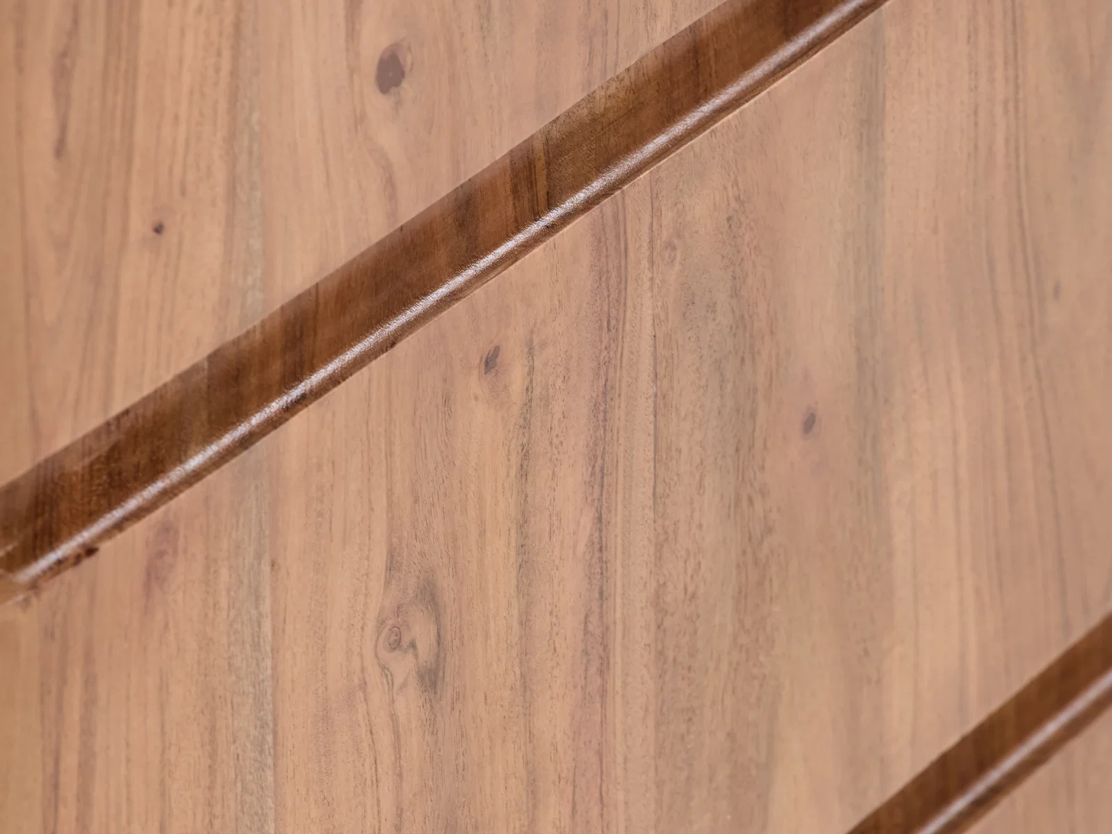 Detailaufnahme der lackierten Akazienholz-Oberfläche des braunen Lowboards Kala, diagonal mit Profilfräsung sichtbar.