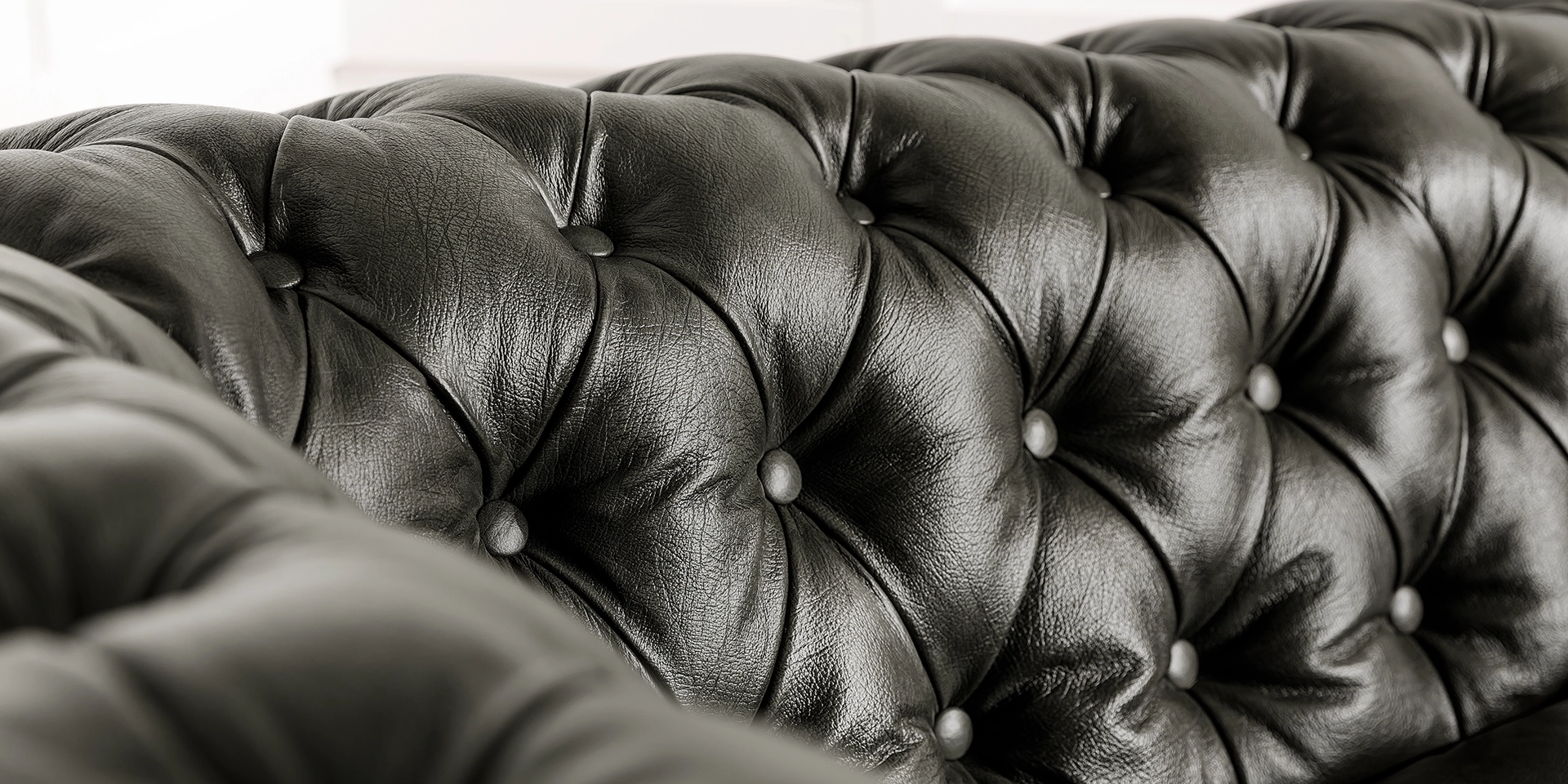 Chesterfield-Detail: Nahaufnahme typischer Knopfheftung, gerollter Armlehne und genarbter Lederoberfläche