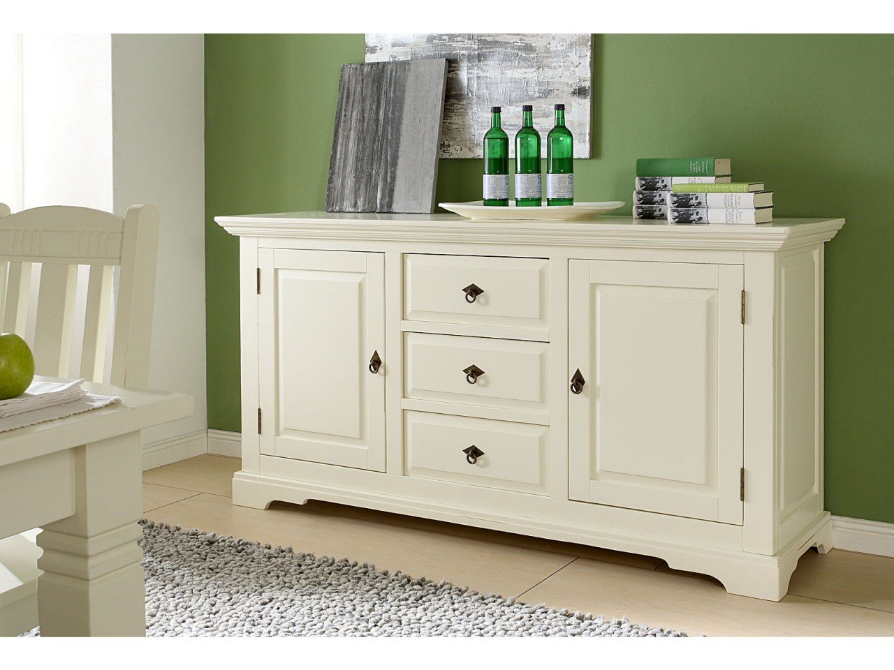 Weißes Sideboard Catana im Landhausstil, mit Pflanzen, Büchern und Deko inszeniert – helles, gemütliches Wohnzimmerambiente