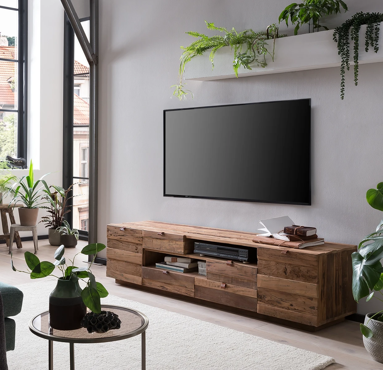 Wohnambiente in einem Wohnzimmer mit naturfarbener TV-Bank, Fernseher, Wandregal und Grünpflanzen