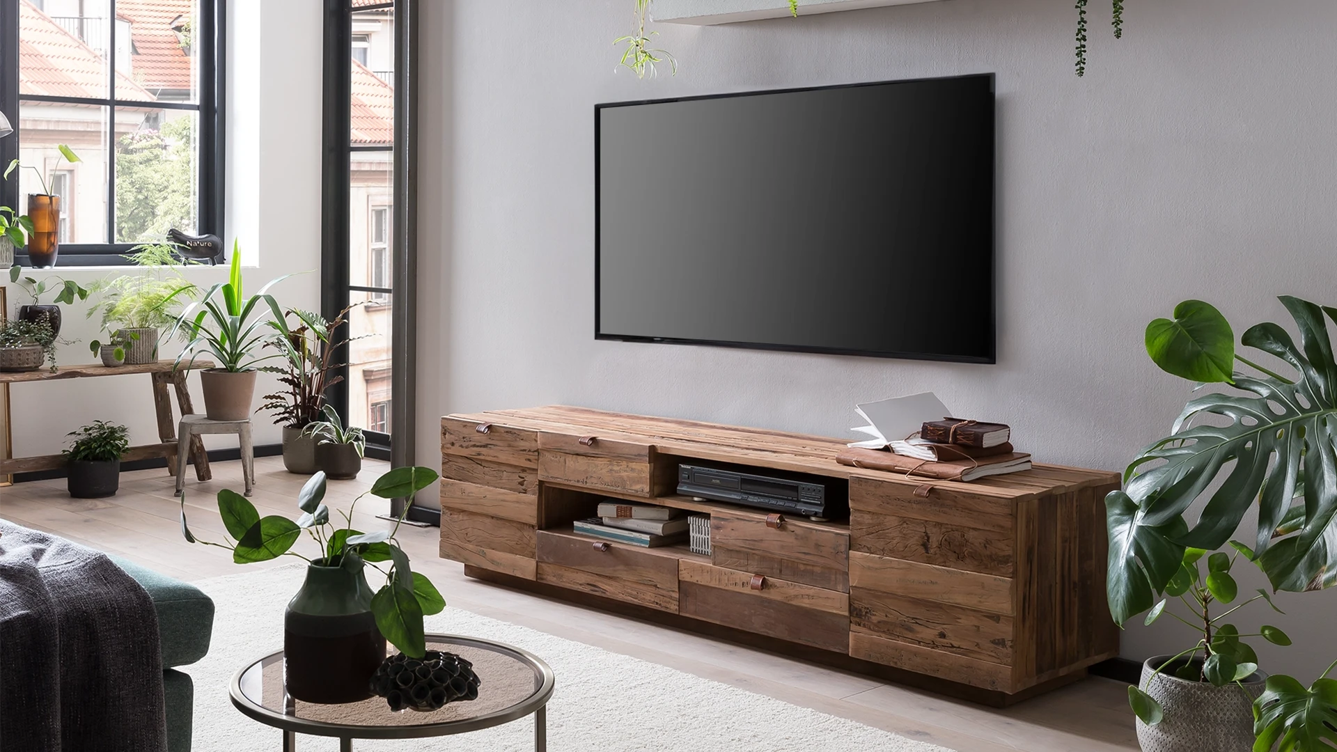 Wohnambiente in einem Wohnzimmer mit naturfarbener TV-Bank, Fernseher, Wandregal und Grünpflanzen