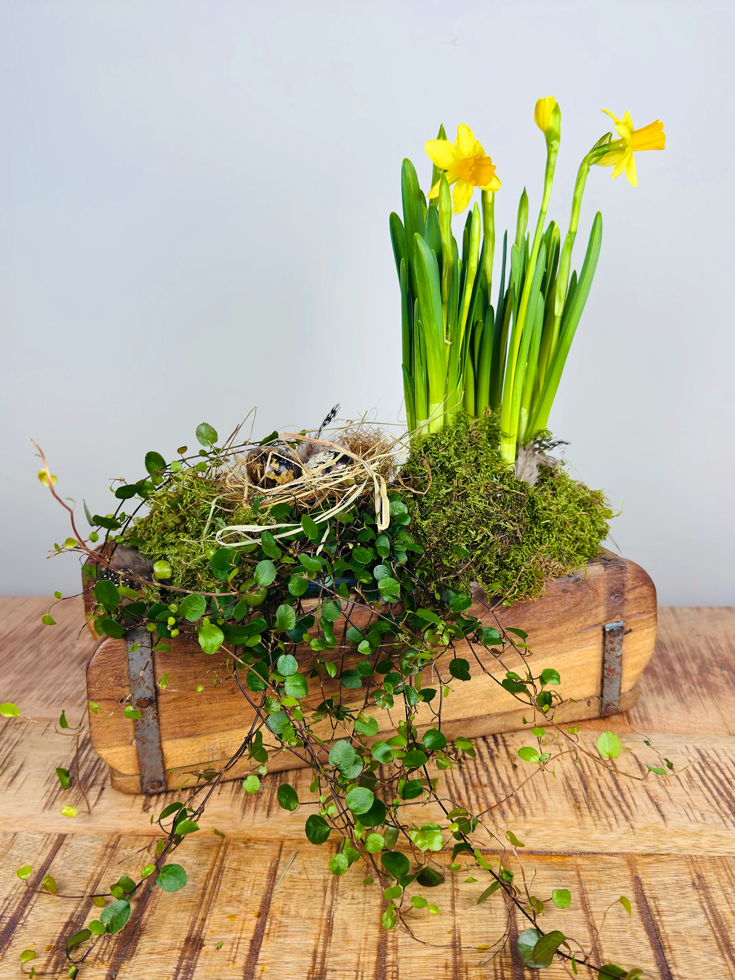 Osterdekoration mit pastellbemalten Eiern auf rustikalem Holztisch, Holzhasen und Frühlingsblumen
