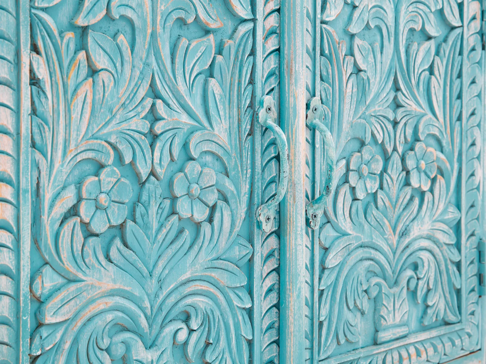 Detailaufnahme eines türkisfarbenen Holzschranks mit floralen Schnitzereien und Griffen im Vintage-Look