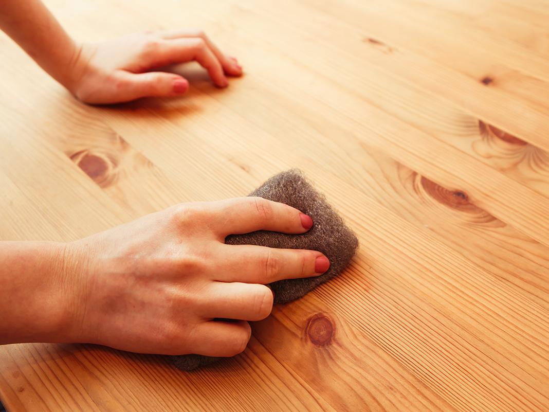 Nahaufnahme: Hand schleift Holzmöbel mit Schleifpapier, sichtbare Holzmaserung und Holzstaub – Renovierung und Aufarbeitung