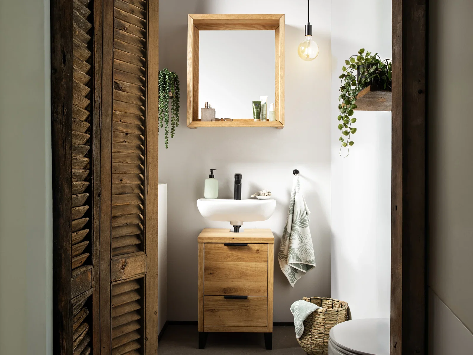 Ambienteaufnahme des ‑ Badmöbelsets „Sydney“ aus warmem Massivholz im modernen Wohnzimmer, dekorativ mit Accessoires und grüner Zimmerpflanze