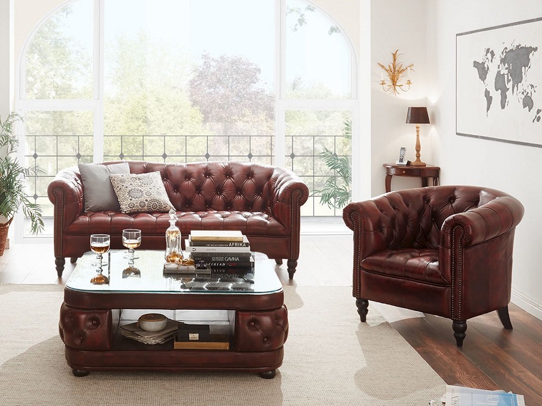 Clubsessel und Clubsofa in gemütlichem Wohnzimmerambiente, dunkles Leder, Holzfußboden und warme Beleuchtung im Vintage-Stil