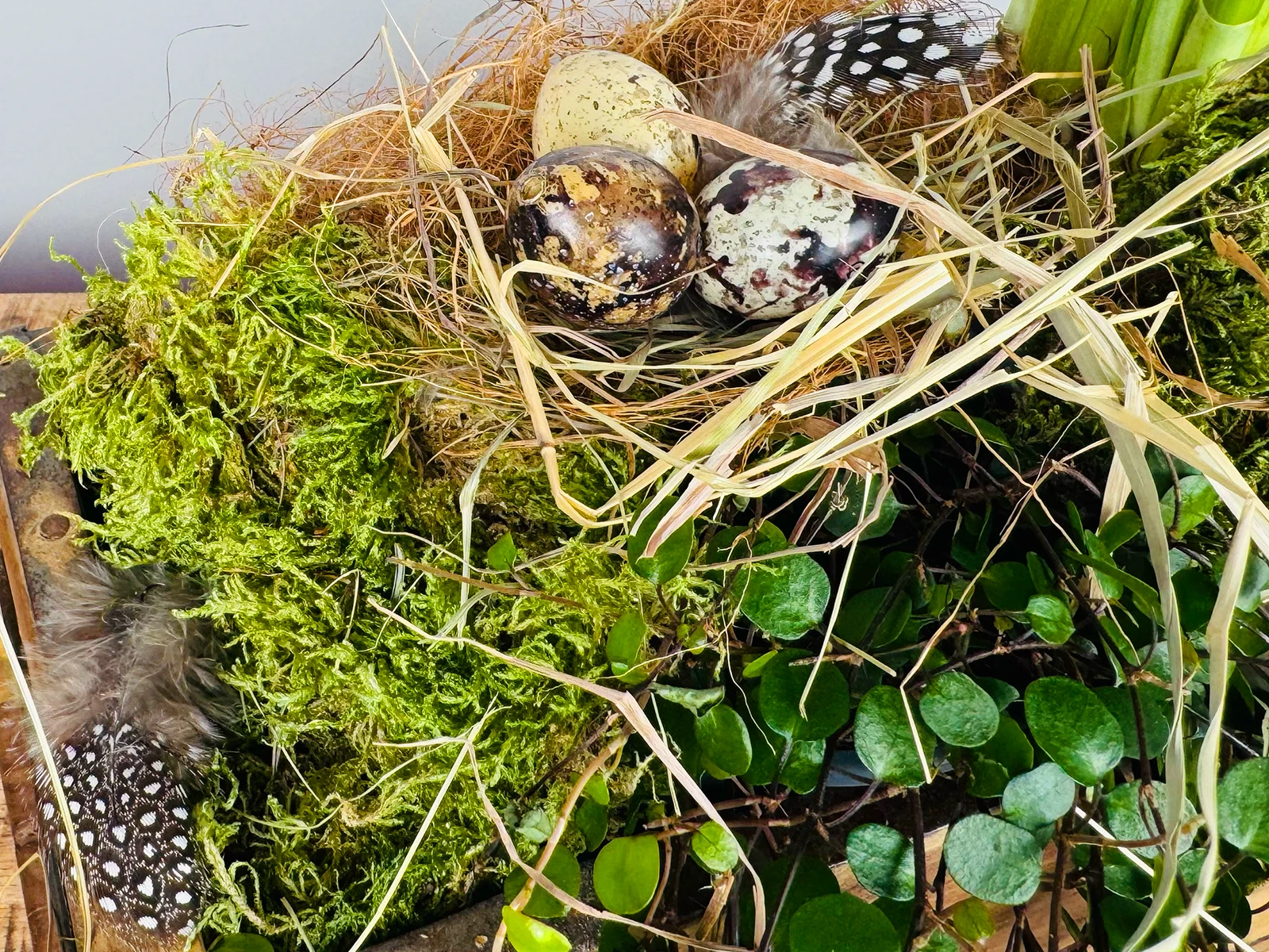 Osterliche Tischdekoration auf Holztisch mit bemalten Eiern, kleinen Holzfiguren und pastellfarbenen Frühlingsblumen
