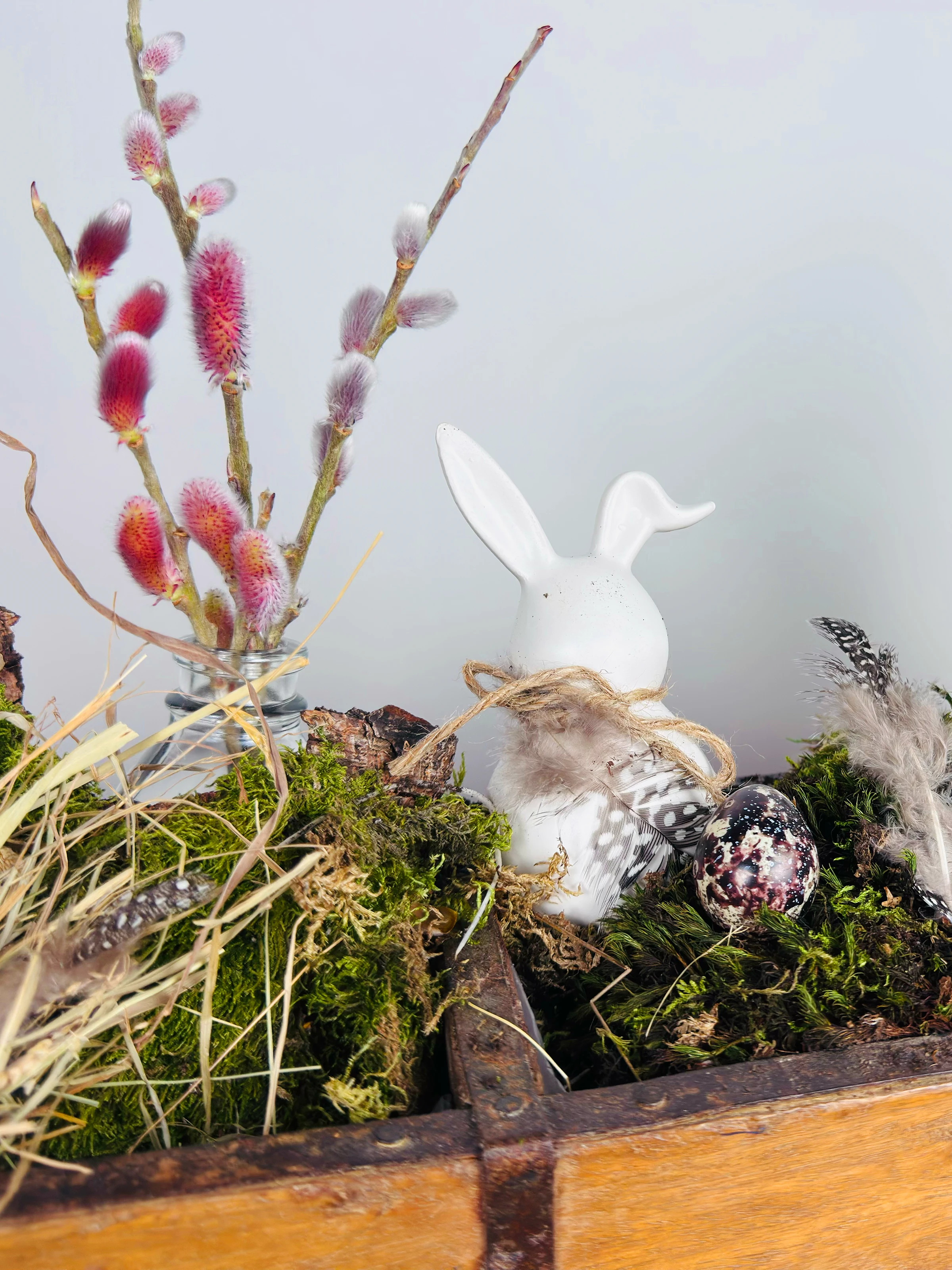 Osterdeko auf hellem Holztisch mit bemalten Eiern, Narzissen und rustikaler Holzdekoration – frühlingshafte natürliche Stimmung
