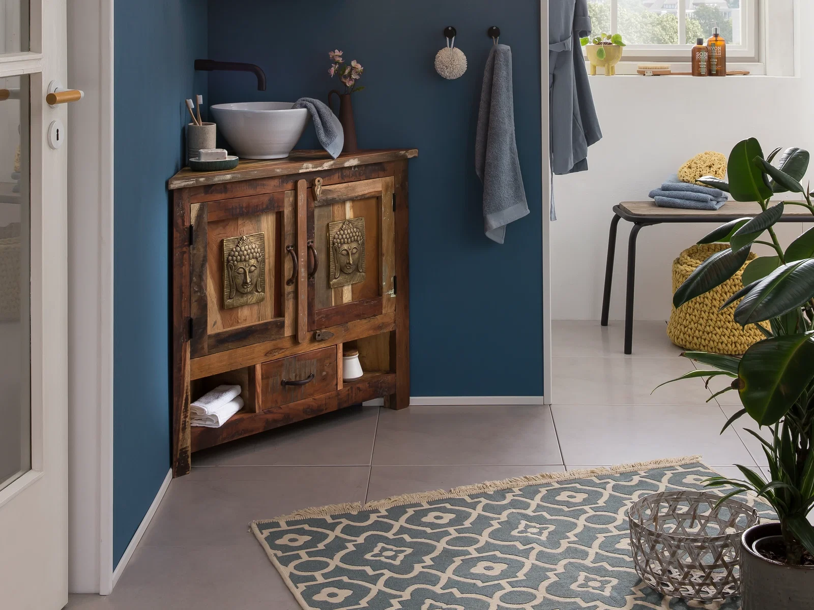 Rustikaler Waschbeckenunterschrank aus Holz im Badezimmer, mit Buddha-Schnitzereien, Aufsatzbecken und blauem Wandambiente